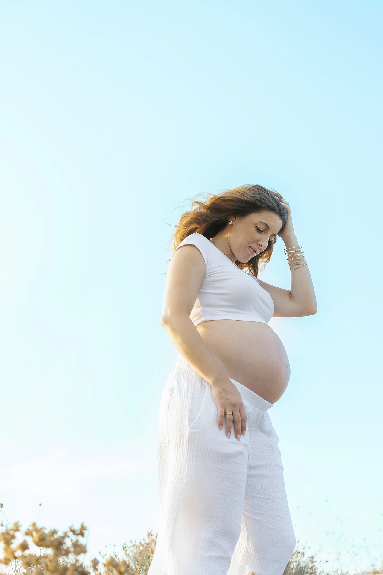 Mujer embarazada en el campo en sesión de fotos premamá con ropa blanca.
