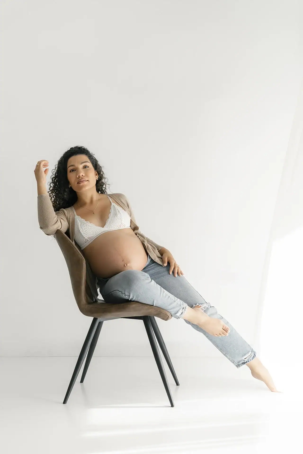 foto de mujer embarazada sentada en estudio de fotos blanco, natural y minimalista con mucha luz.