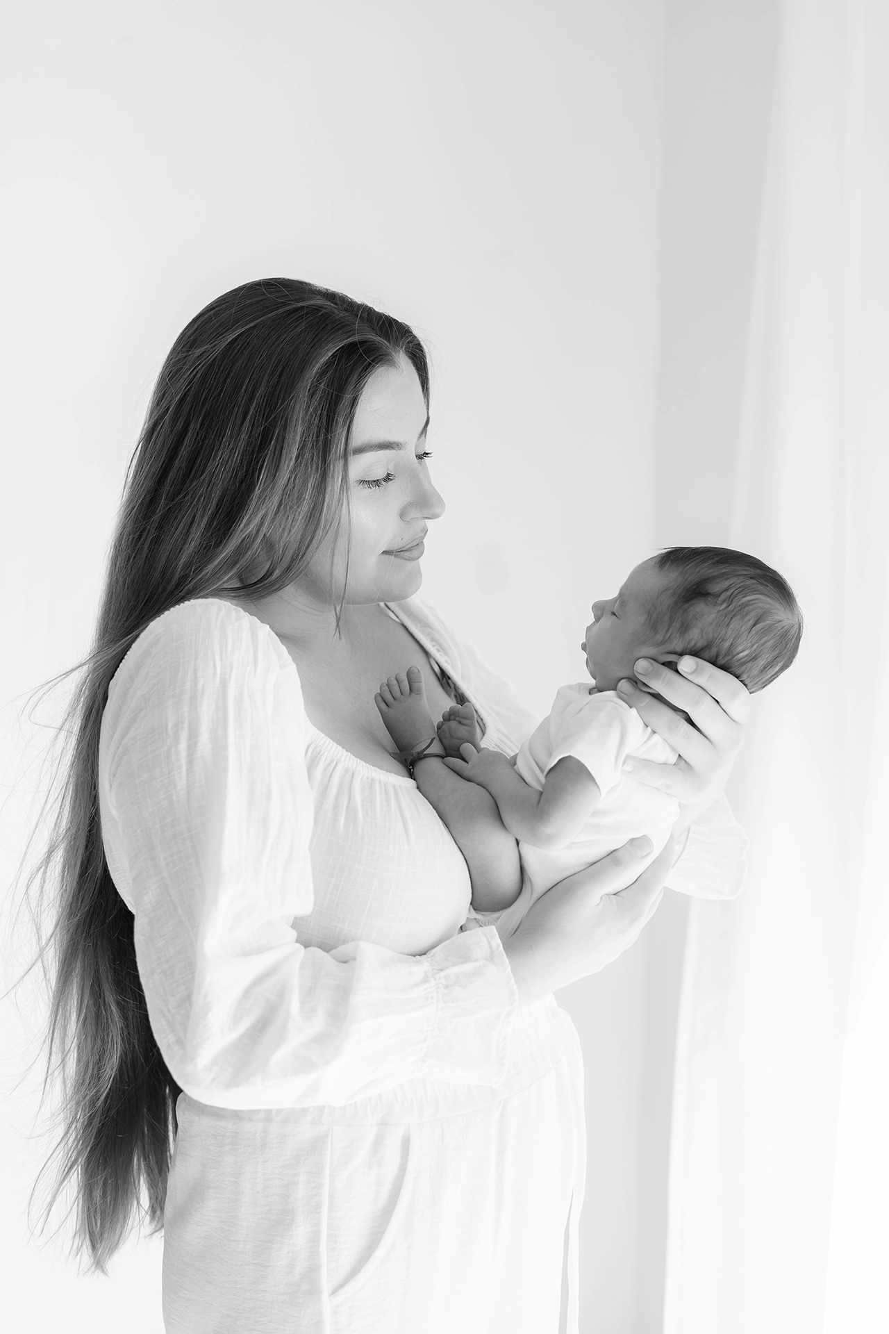 Recién nacido fotografía en familia- Silla Valencia Fotografía de recién nacido en los brazos de su madre, con iluminación suave, en estudio de Silla, Valencia.