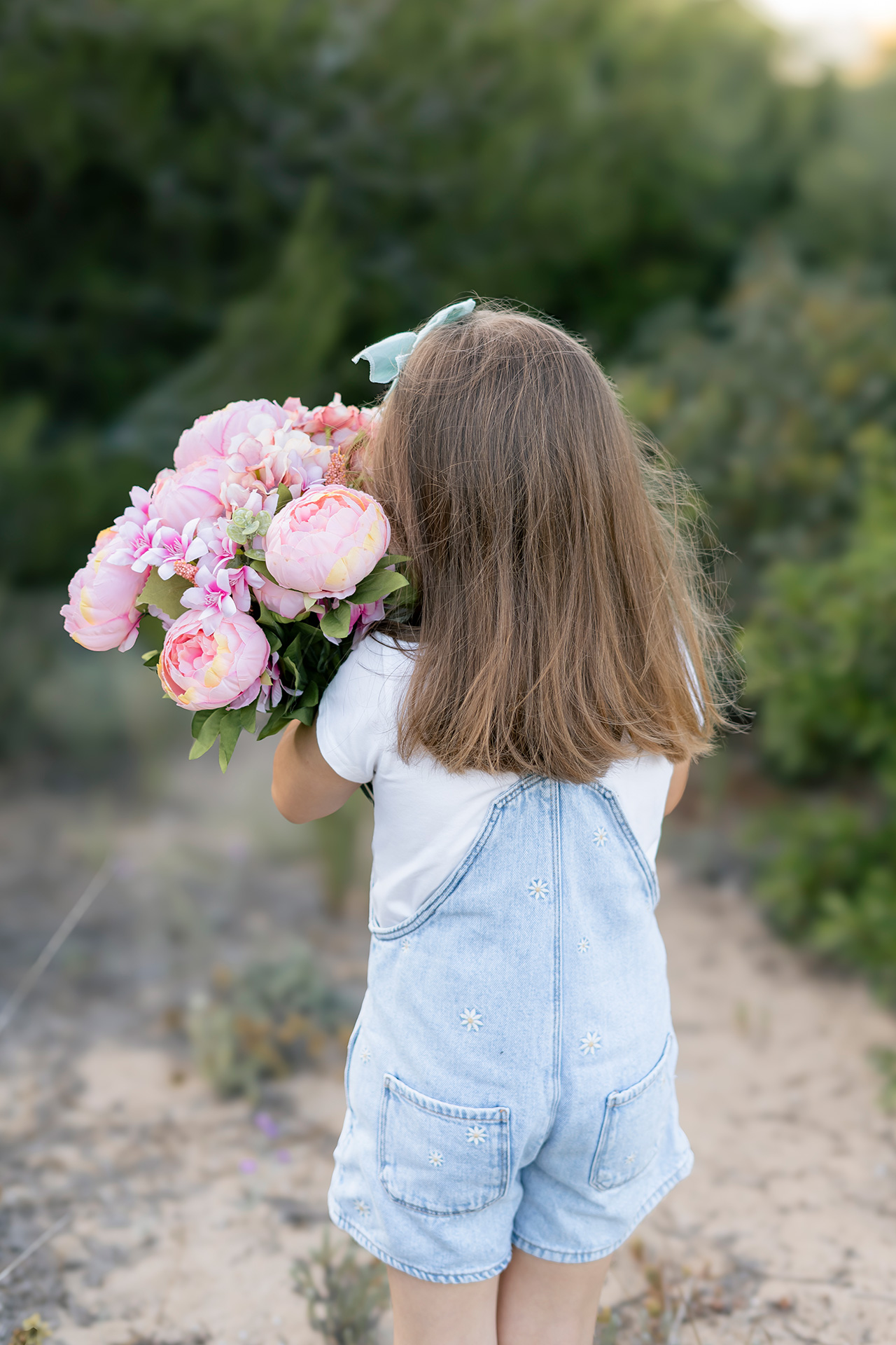 Fotos en exteriores Valencia. Fotógrafo de familias foto de una niña de espaldas cargando un ramo de flores rosas en la playa