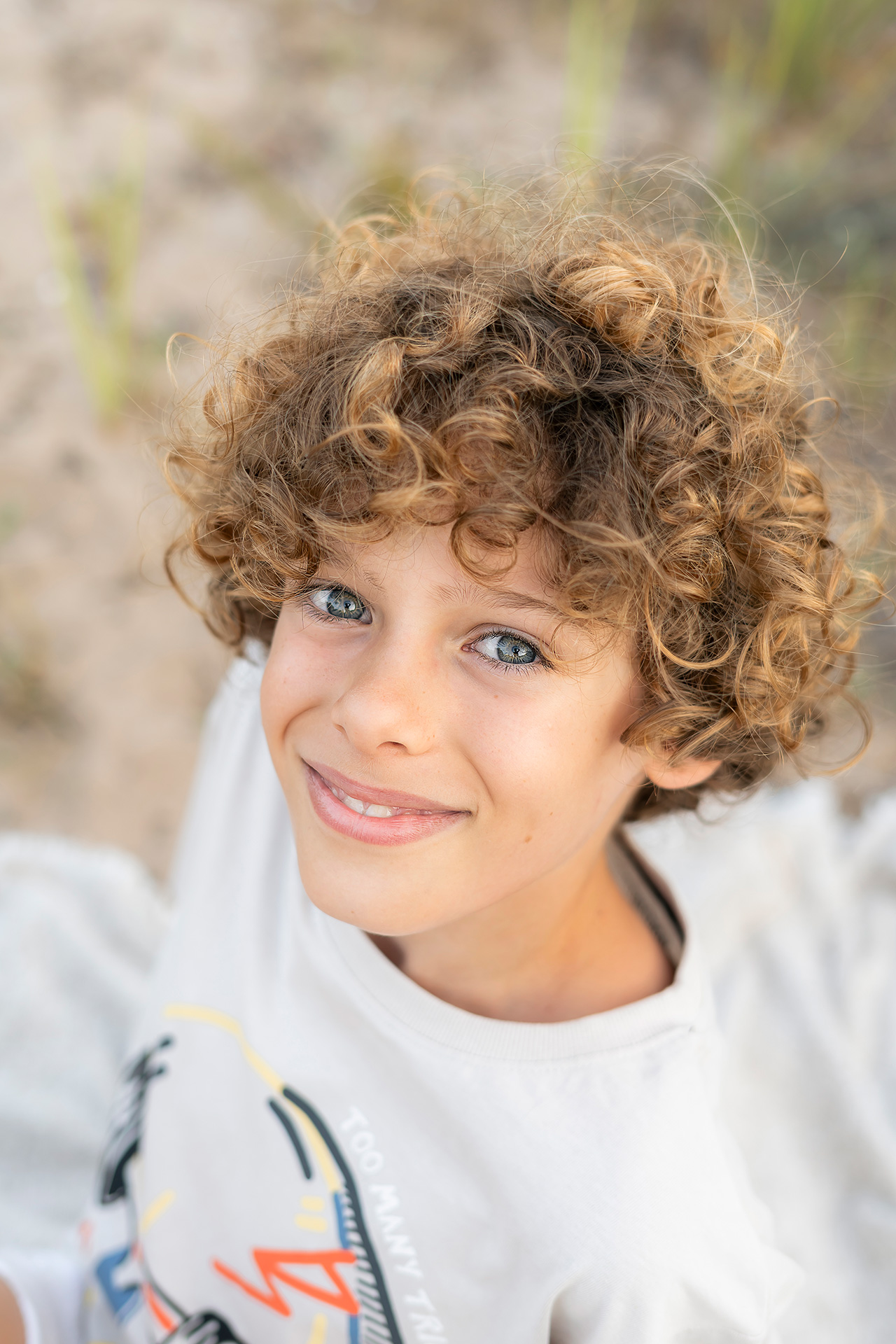 Sesión de fotos infantil y familiar en exteriores valencia Foto de un niño mirando a cámara primer plano, niño rubio de rizos en la playa valencia