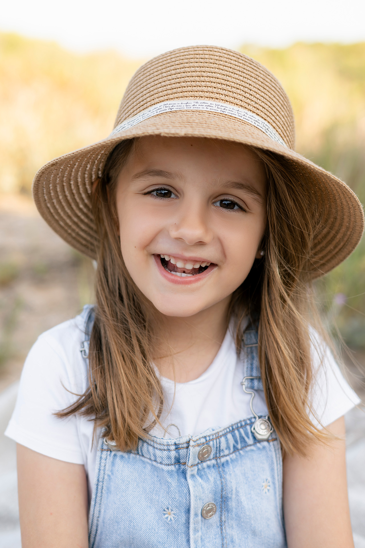 Fotos de familia exterior, fotógrafo de familias en Valencia Foto de una niña sonriendo con un sombrero en la playa, estilo de fotos natural y minimalista