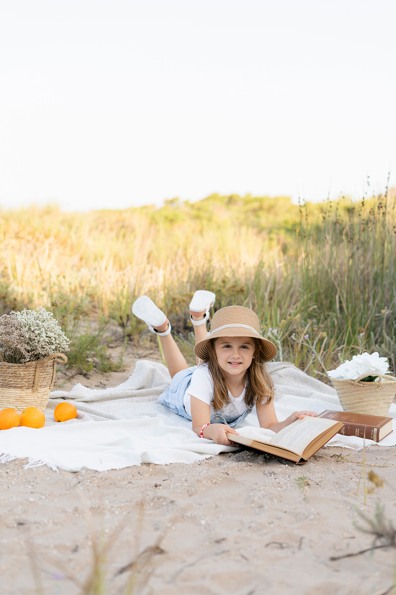 Sesión de familias en exterior Valencia Foto de una niña en la playa de valencia, estilo natural. niña con sombrero leyendo un libro en exteriores