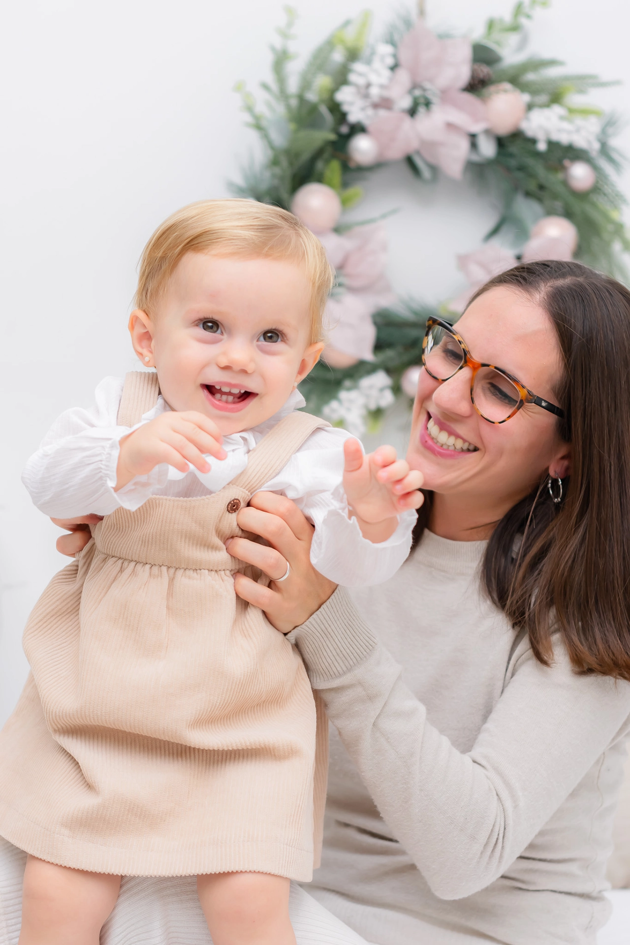 Sesión de fotos de Navidad infantil en Valencia 2024 Bebé junto a su madre vestido con ropa navideña sobre set minimalista en estudio de fotografía