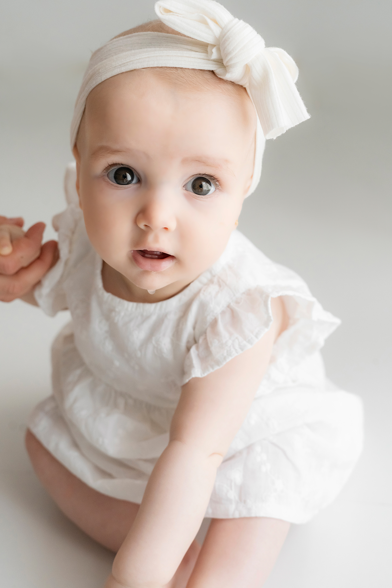 foto de un bebe de 8 meses sentado con vestido blanco y diadema con lazo