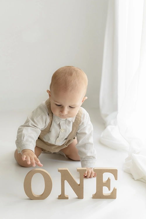Bebé celebrando su primer cumpleaños junto a cartel one en el estudio de fotografía.