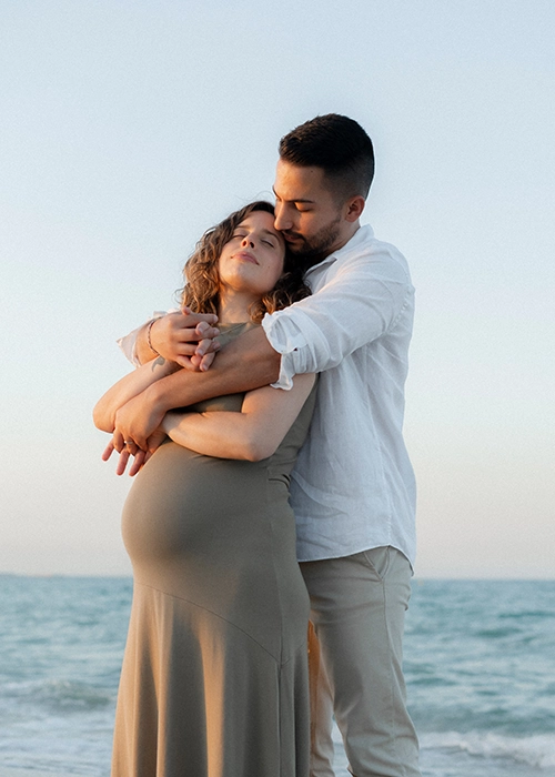 foto de pareja embarazados abrazados en la playa al atardecer