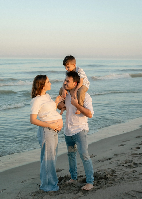 familia en la playa sonriendo al atardecer mujer embarazada y niño a los hombros del padre