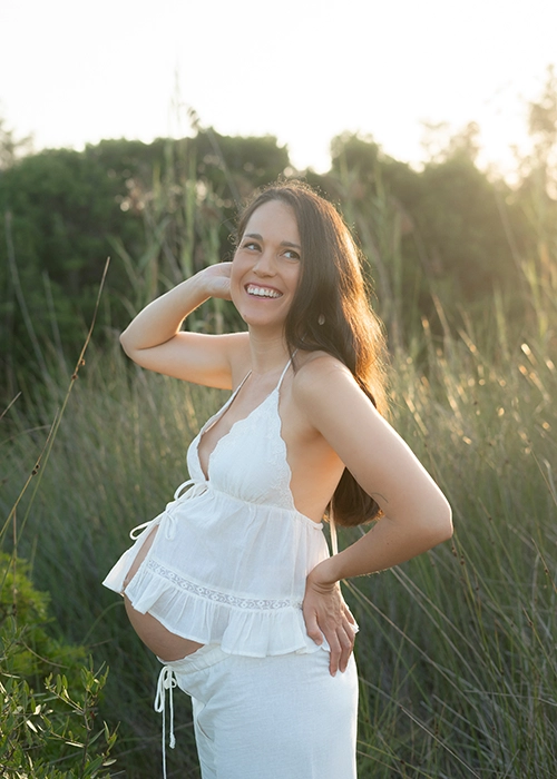 foto de mujer embarazada en exterior al atardecer con pantalón blanco y blusa con tirantes