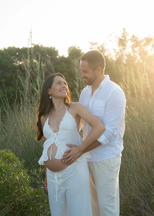 foto de pareja embarazada mirándose a los ojos al atardecer en exterior