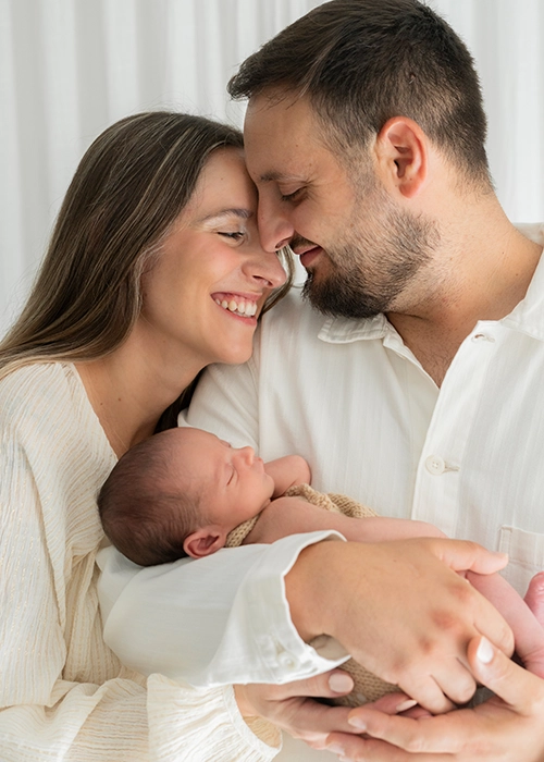 foto de pareja mirándose sosteniendo en brazos a su bebe recien nacido