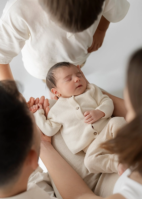 bebe dormido sobre las piernas de la madre y familia mirándolo