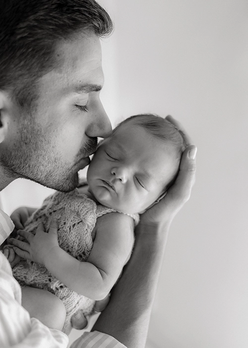 padre dando un beso en la mejilla a su bebe recien nacido dormido